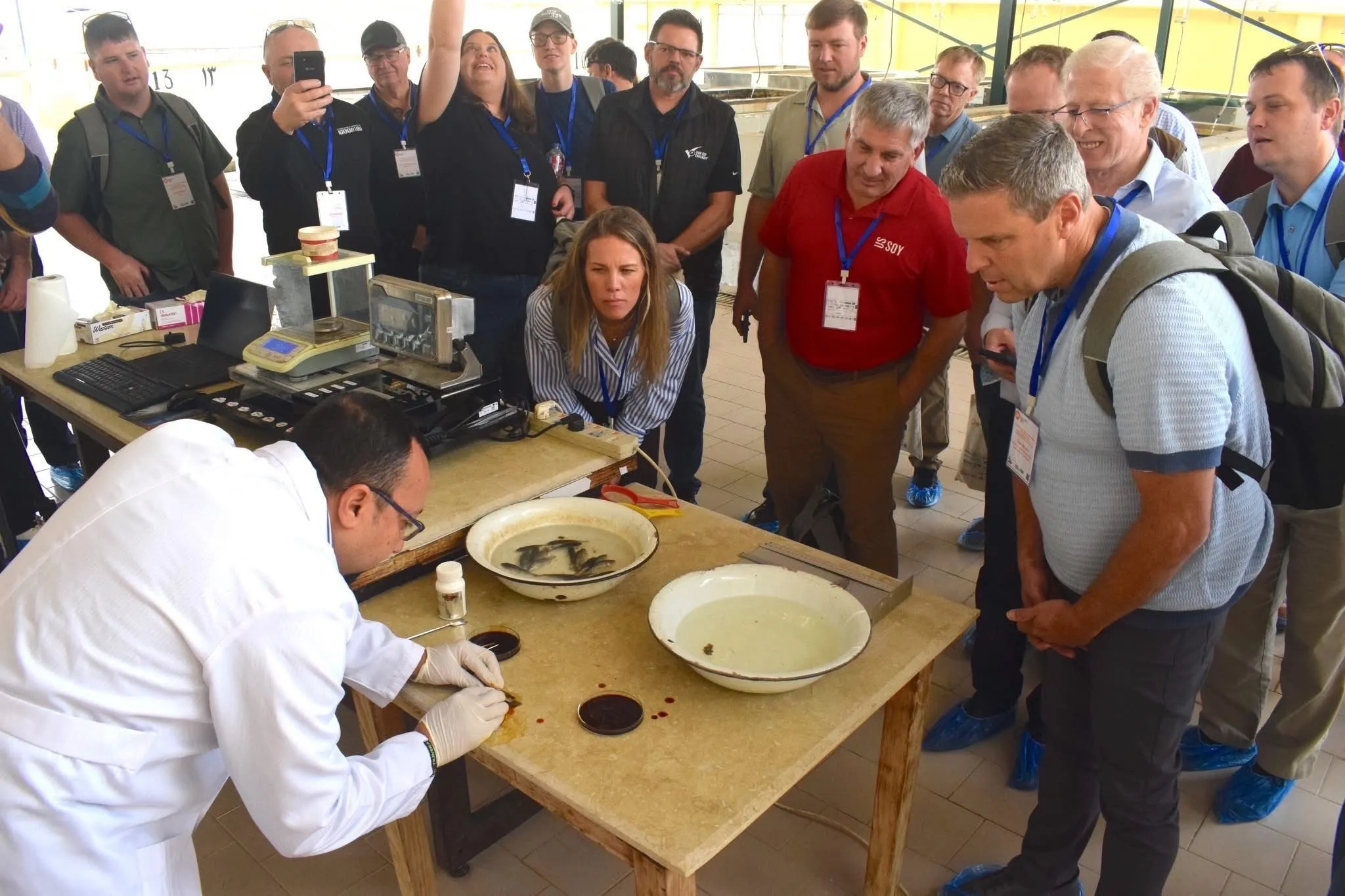 Group of people observing a technician in a lab coat conducting a fish analysis demonstration at a table.
